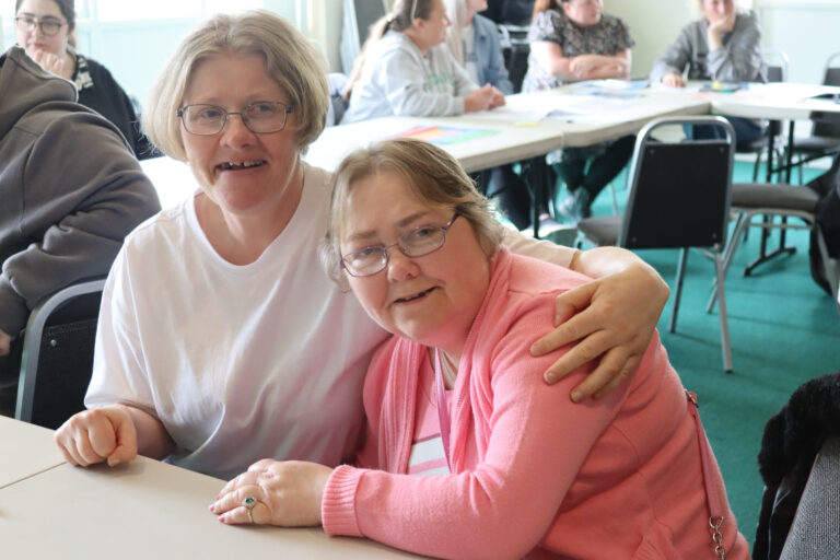 Two members of supported living sat at a table smiling