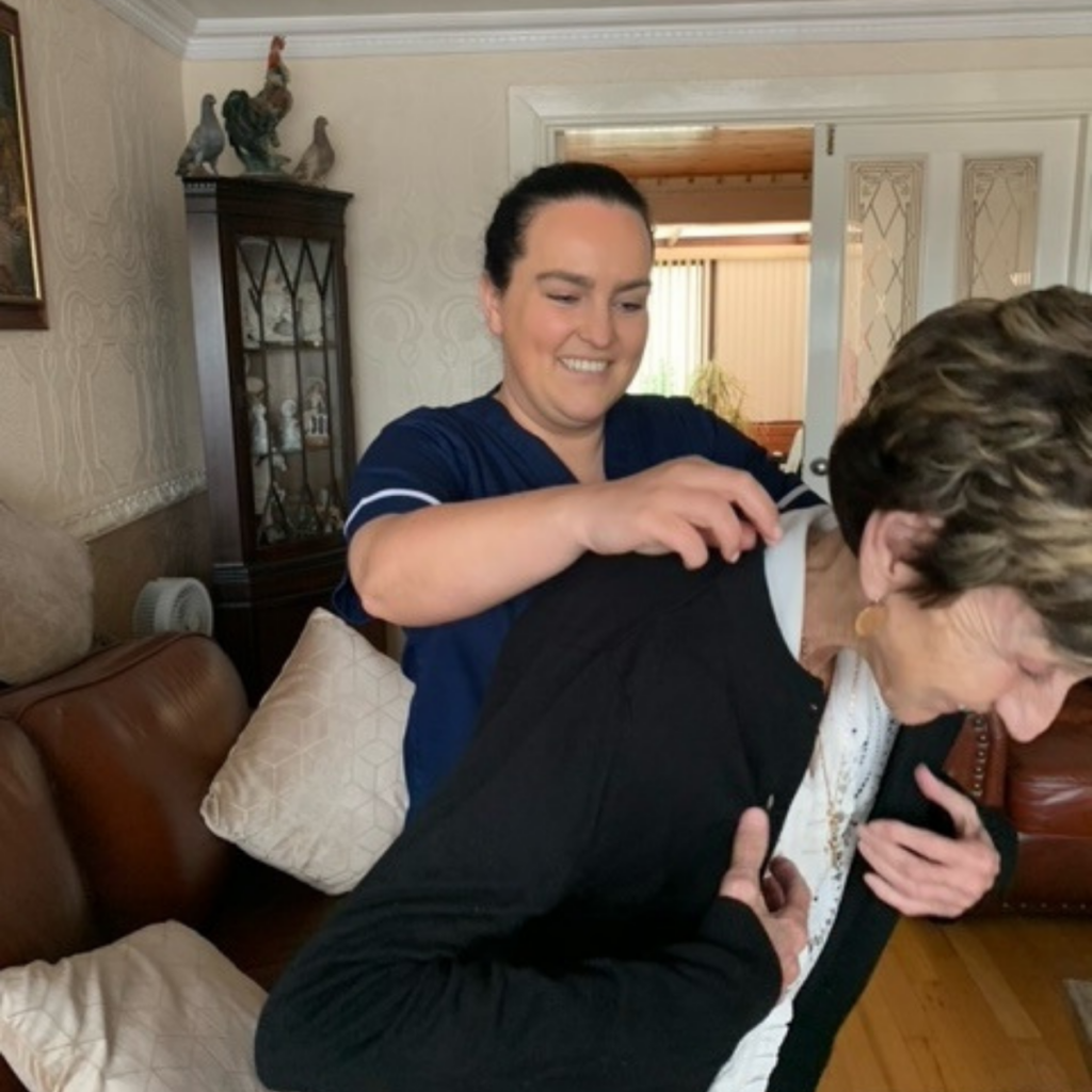 Reablement Worker helping woman put on cardigan.