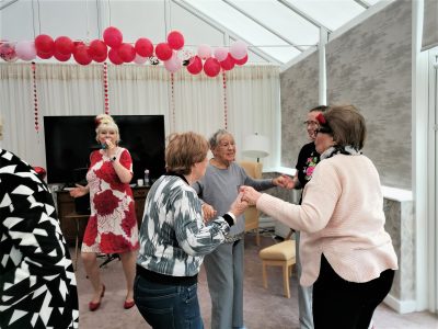 Jean dancing at a party with friends and a woman singing