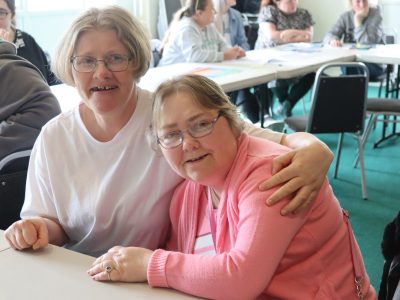 Two members of supported living sat at a table smiling