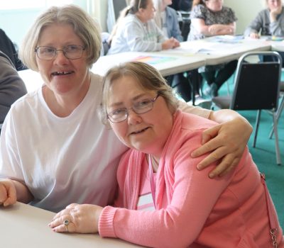 Two members of supported living sat at a table smiling